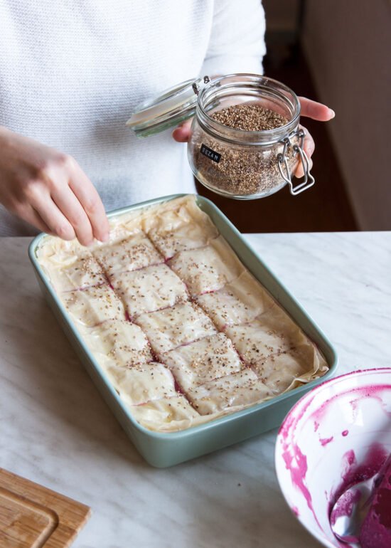 Ruke posipaju sjemenke preko nepečene pite od cikle i ricotte