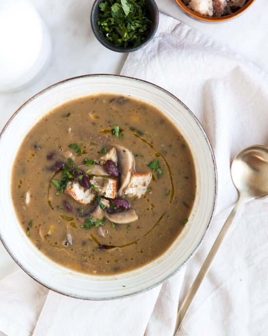 Kremasto varivo od gljiva i graha u bijelom tanjuru, posluženo s gljivama i krutonima od kruha