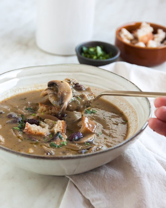 Kremasto varivo od gljiva i graha u bijelom tanjuru, posluženo s gljivama i krutonima od kruha