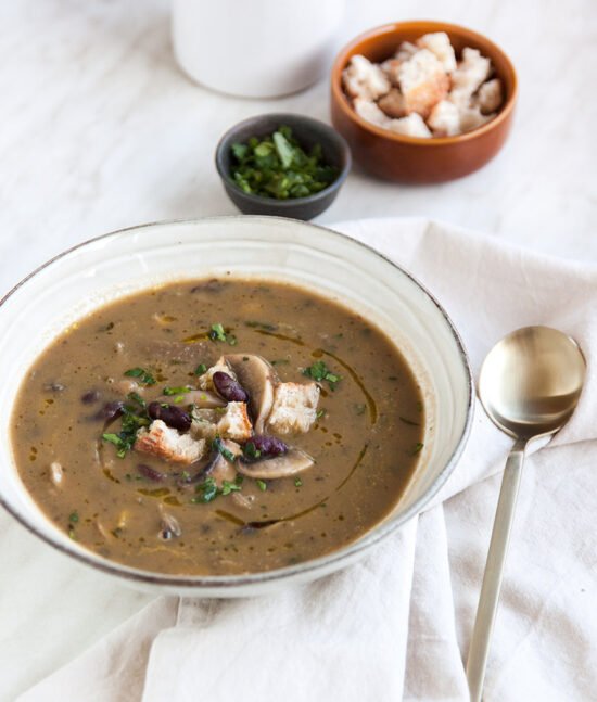 Kremasto varivo od gljiva i graha u bijelom tanjuru, posluženo s gljivama i krutonima od kruha