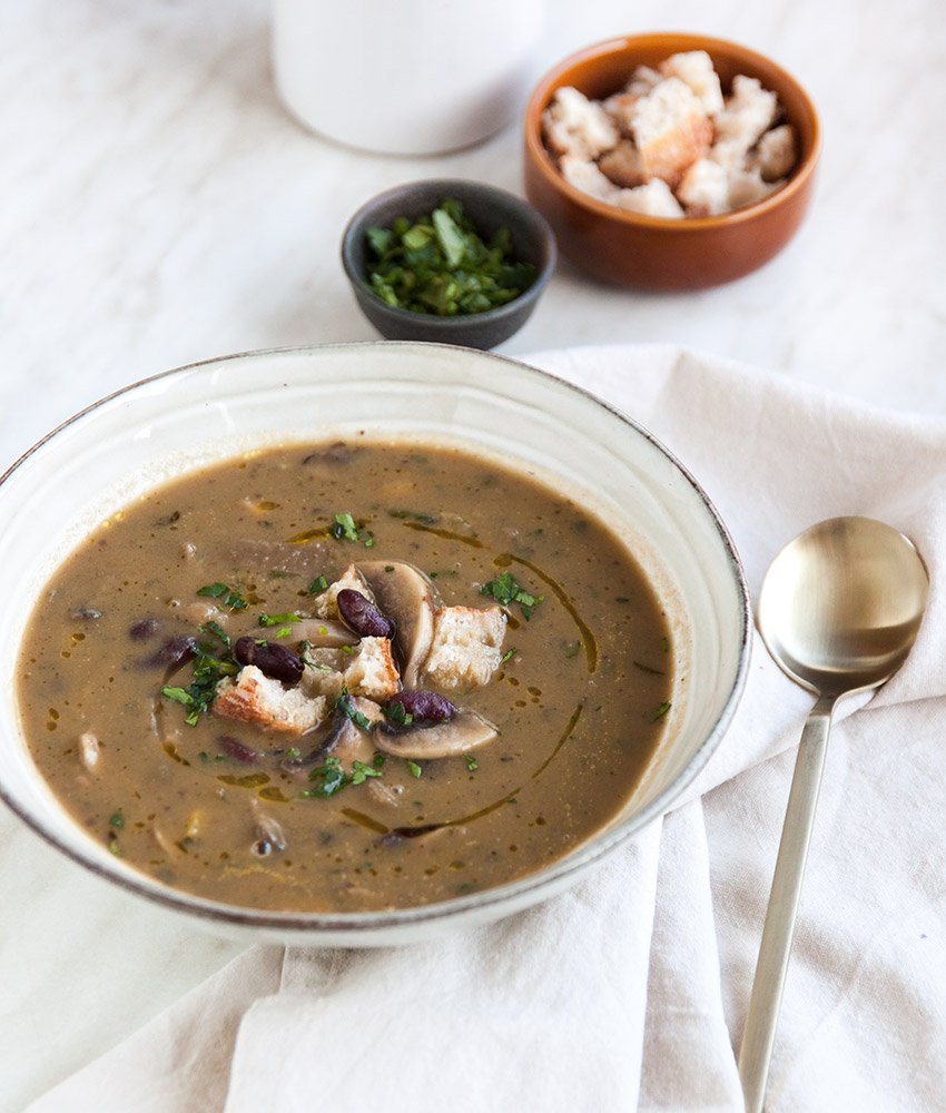 Kremasto varivo od gljiva i graha u bijelom tanjuru, posluženo s gljivama i krutonima od kruha